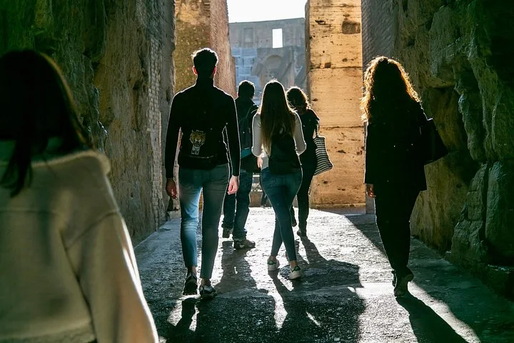 Visitors walking through a sunlit Colosseum corridor