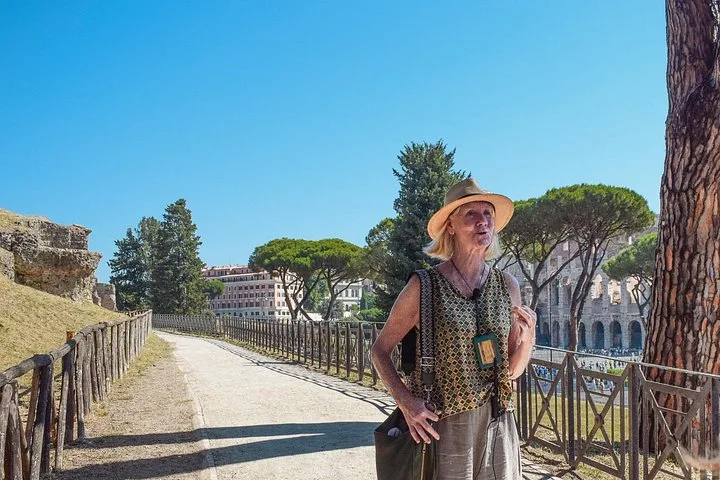Guide on a pine-lined archaeological path with the Colosseum in the distance