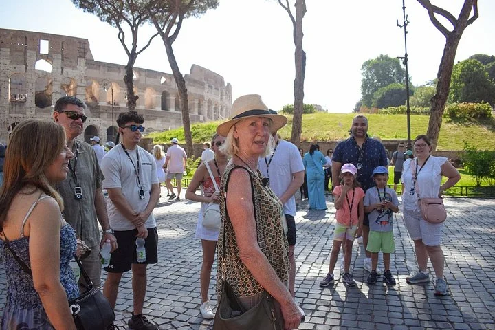 Guide speaking to visitors among pines beside the Colosseum