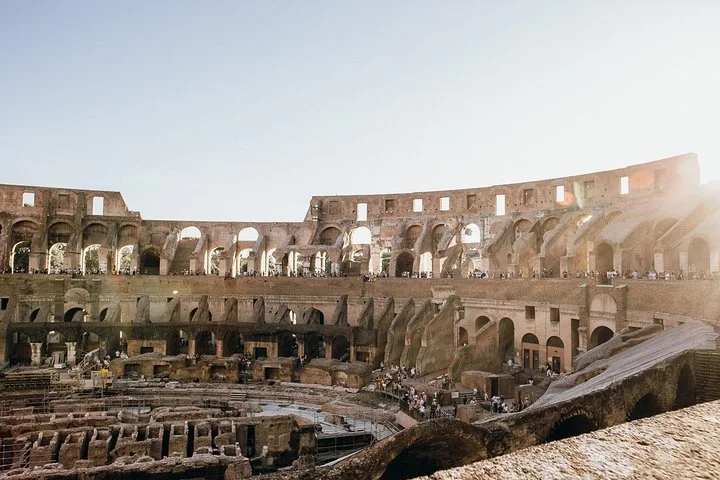 Warm sunlight illuminates the Colosseum's interior arches and arena.
