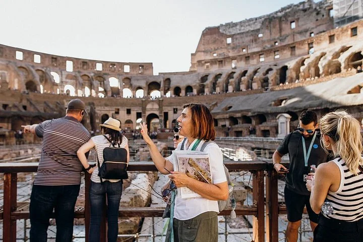 A guide explains the amphitheatre beside the arena's wooden railing.