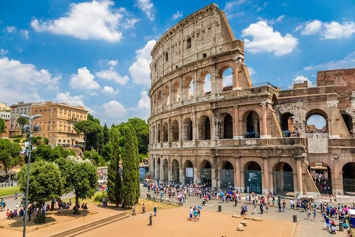 Bright Colosseum exterior with green trees and a vivid blue sky
