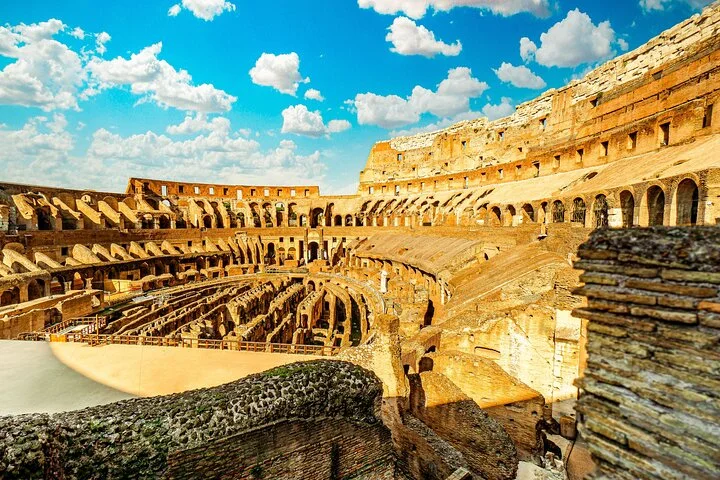 Golden stone arches surround the Colosseum arena beneath a blue sky.