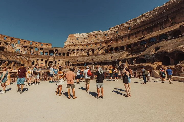 Visitors stand on the Colosseum arena floor beneath its ancient tiers.