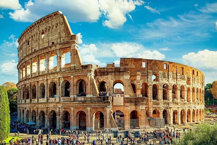 Golden Colosseum exterior beneath vivid blue sky and clouds
