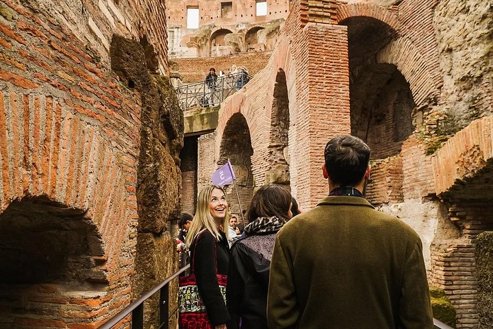 A guide leads visitors between deep brick walls beneath the Colosseum arena.