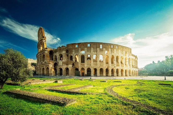 Colosseum exterior above green lawns in strong afternoon light