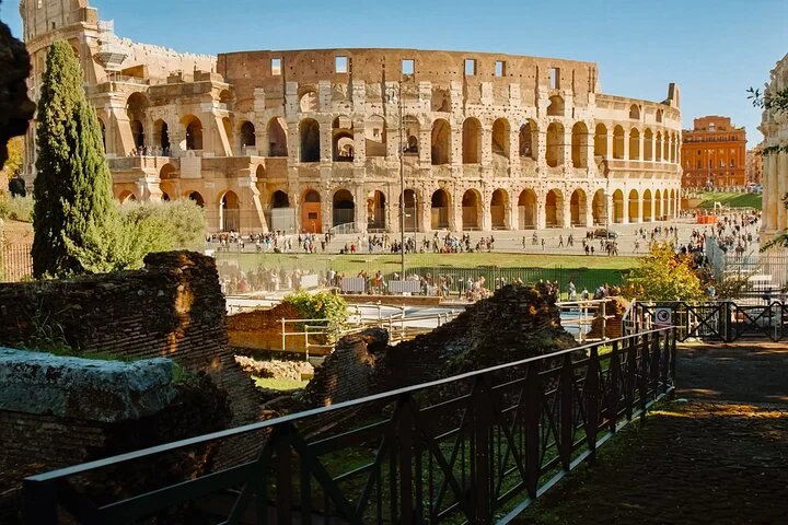 Colosseum exterior seen across a shaded archaeological path