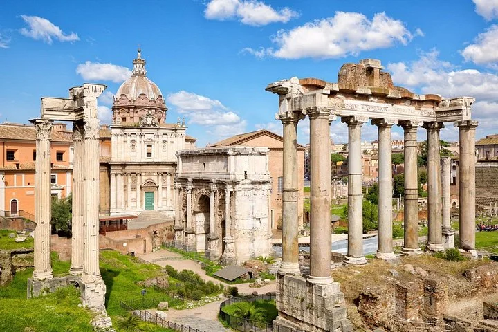 The Temple of Saturn's columns stand in the Roman Forum beneath blue skies.