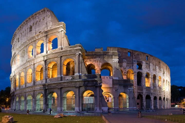 The illuminated Colosseum facade stands beneath a deep blue evening sky.