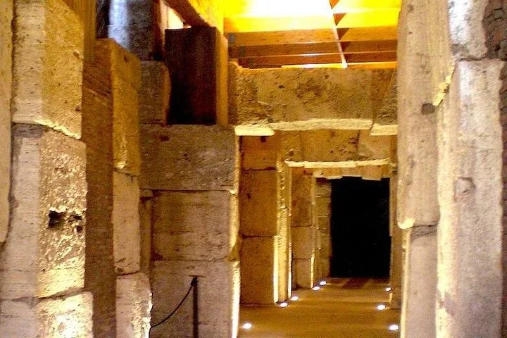 Golden light illuminates stone pillars in a corridor beneath the Colosseum arena.
