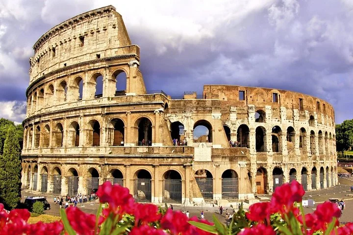 Colosseum exterior framed by red flowers beneath clouds
