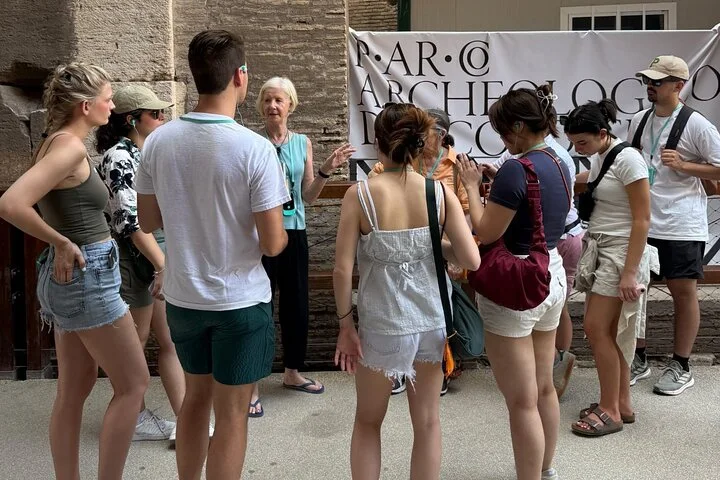 A guide talks with visitors near a Colosseum information banner.
