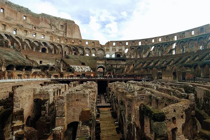 The Colosseum's exposed underground walls fill the foreground beneath its tiers.