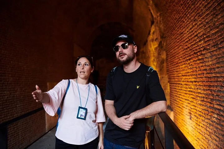 A guide and visitor walk through a brick-arched underground corridor.