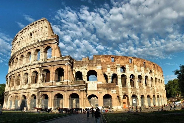 The Colosseum facade stands beneath blue skies and textured white clouds.