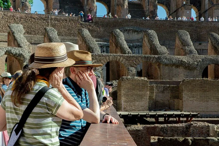 Visitors listen beside the Colosseum arena railing.