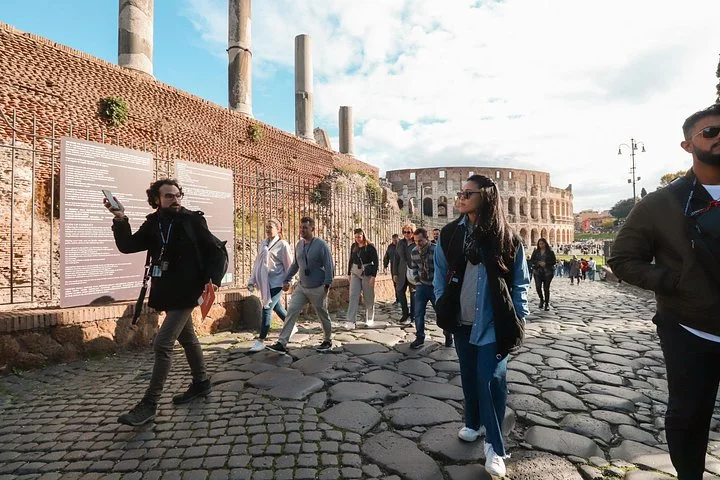 Guide and visitors walking on an ancient Forum path with the Colosseum behind