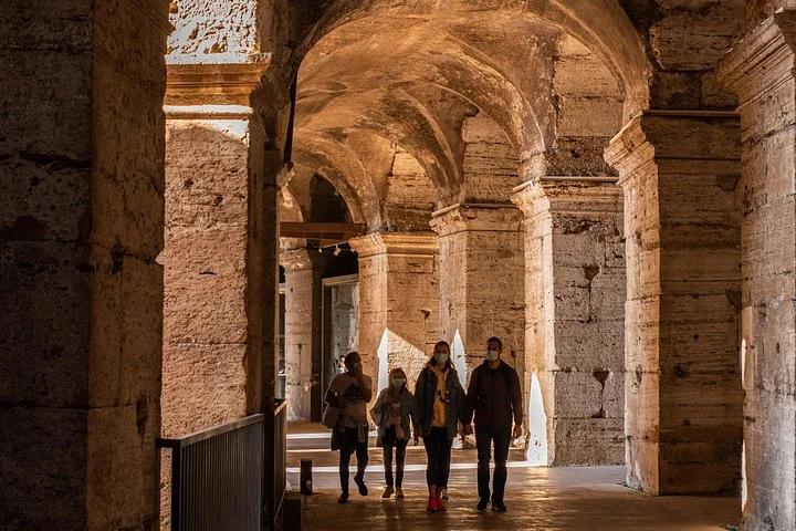 Visitors walking beneath the warm brick vaults of a main Colosseum arcade