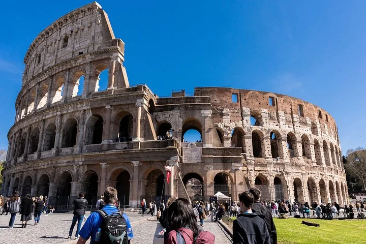 Visitors approaching the Colosseum exterior beneath a vivid blue sky