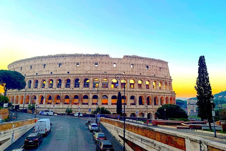 The Colosseum facade is illuminated beneath a blue evening sky.