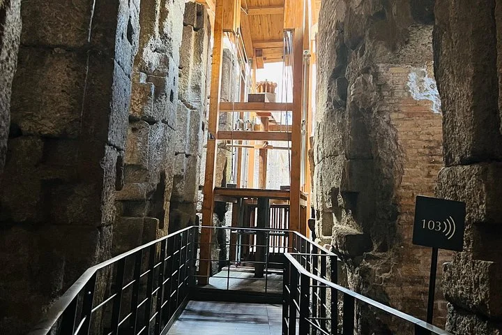 A reconstructed timber lift stands between stone walls beneath the Colosseum arena.
