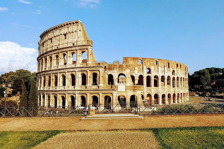 Colosseum exterior above grass beneath a blue sky