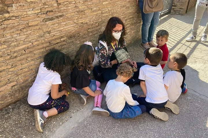 Guide leading a seated children's activity beside ancient Colosseum brickwork
