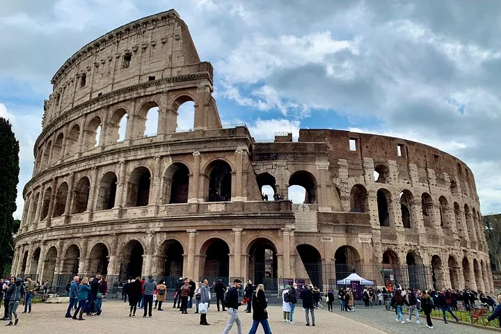 Colosseum exterior and visitors beneath a cloudy sky