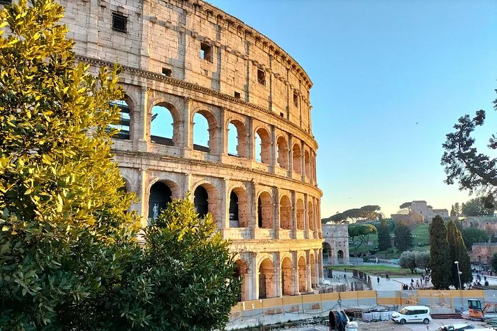 Golden light on the Colosseum exterior beside green trees