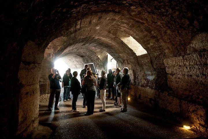 A guide and visitors gather beneath an underground arch in the Colosseum.