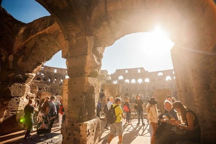 Visitors move through a sunlit archway inside the Colosseum.