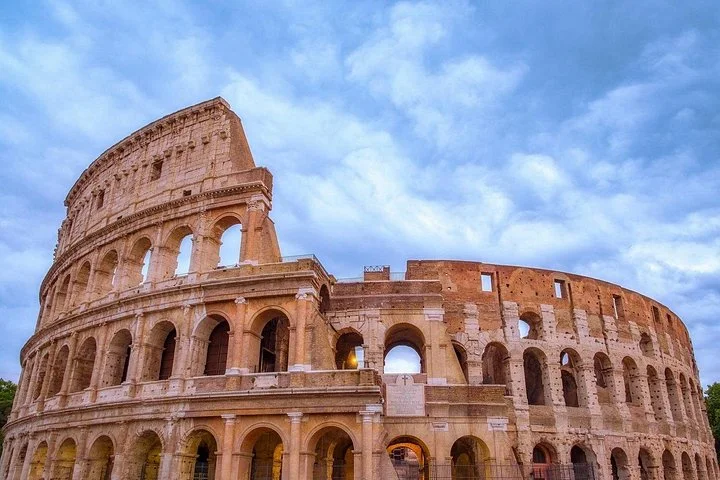 Upward view of the Colosseum facade beneath a cloudy sky