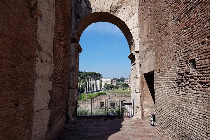 Colosseum arch framing blue sky and distant ancient columns