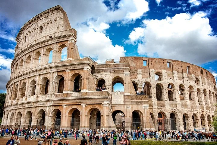 Colosseum exterior beneath vivid blue sky and large white clouds
