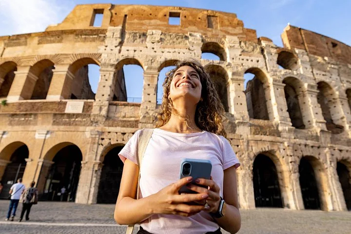 Visitor looking up at the Colosseum exterior while holding a phone