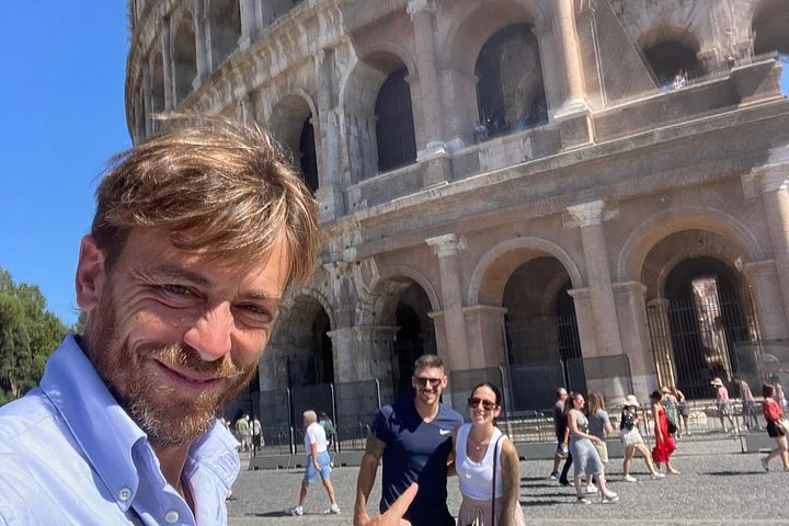 A guide and visitors outside the Colosseum arches