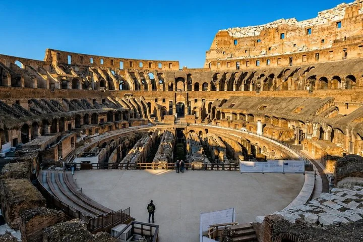 The Colosseum interior glows in sunshine beneath a deep blue sky.