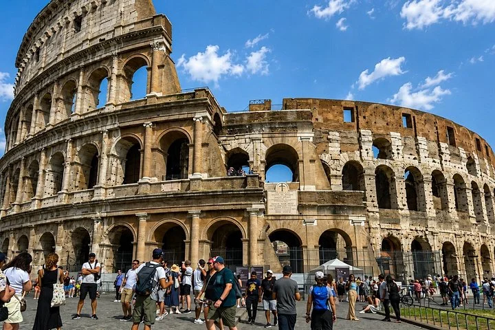 Visitors gather below the Colosseum's sunlit outer arches.