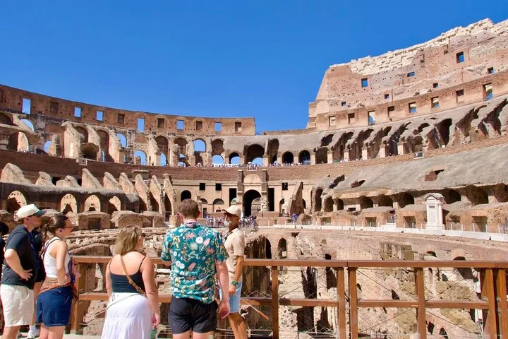 A guide speaks with visitors beside the Colosseum arena railing.
