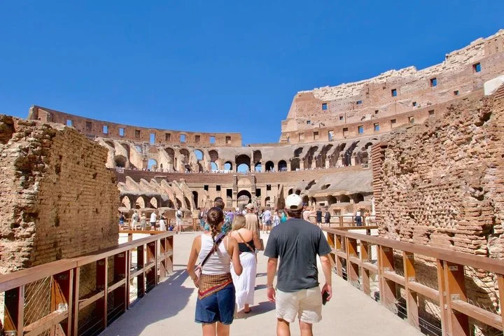 Visitors walk onto the Colosseum arena beneath a clear blue sky.