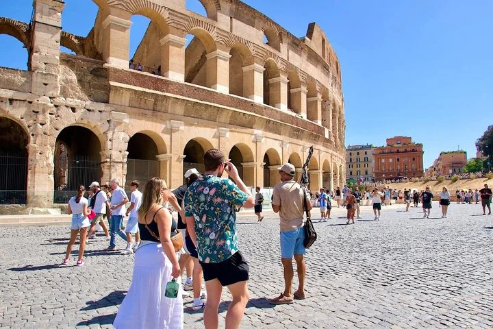 Visitors cross the plaza beside the Colosseum facade.