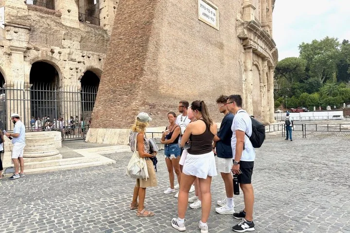 A guide speaks with visitors beside the Colosseum entrance.