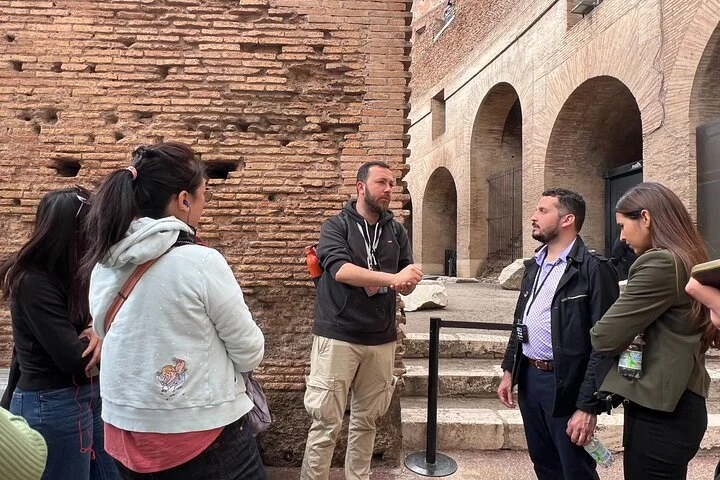 A guide speaks with visitors beside the Colosseum's brick walls.