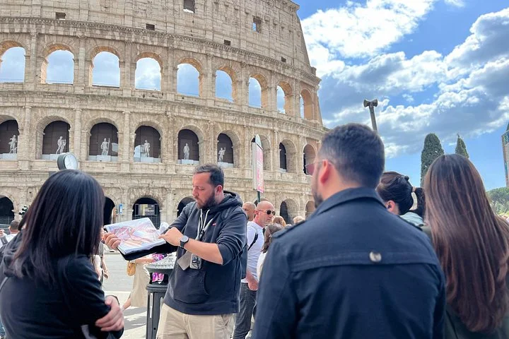 A guide and visitors stand outside the Colosseum beneath blue skies.