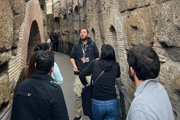 A guide walks along a narrow passage between the Colosseum's underground walls.