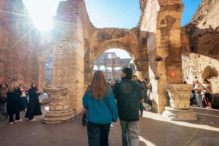 Visitors walking through a sunlit Colosseum arcade