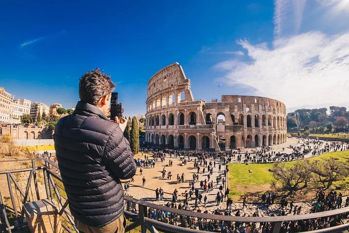 A visitor photographs the Colosseum beneath a clear blue sky.