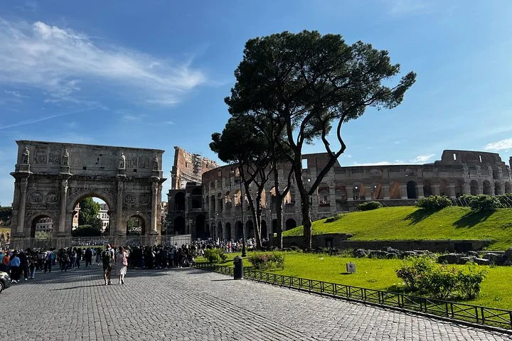 The Arch of Constantine and Colosseum beside green lawns and an umbrella pine.