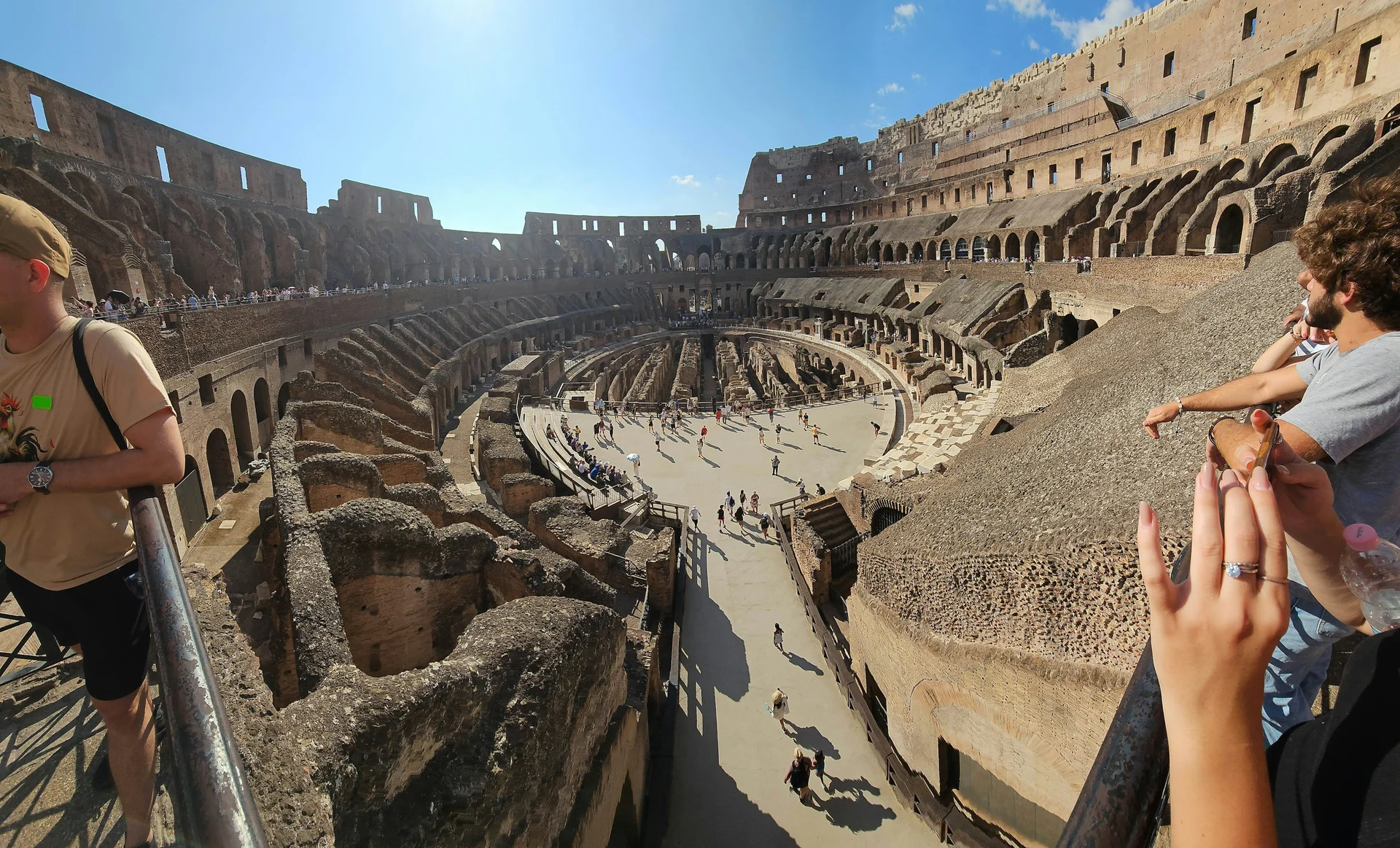 Visitors on the arena floor inside the Colosseum under a blue sky